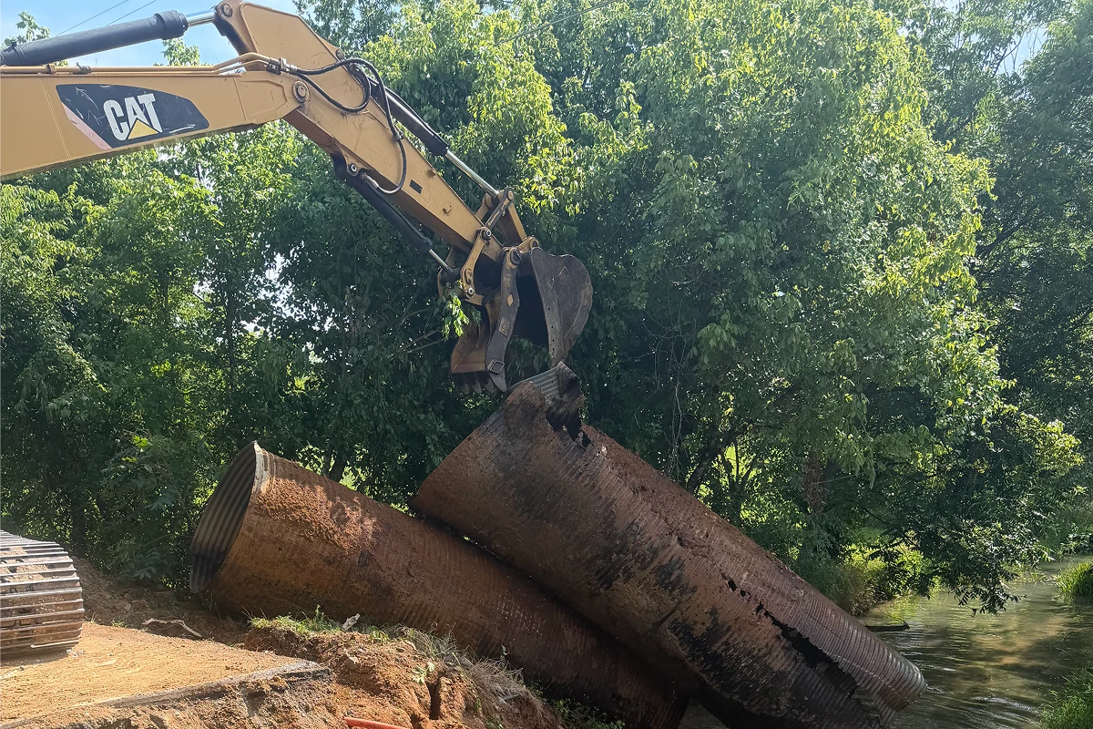 Excavator lifting large rusty pipes